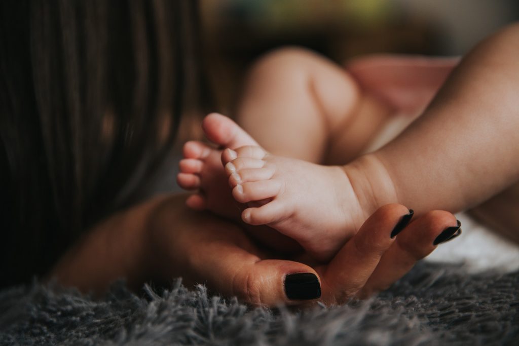 Woman dark hair holding baby feet in her hands.