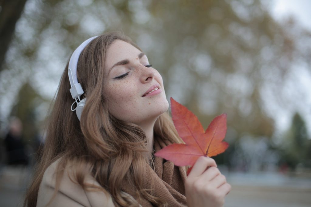 Woman wearing headphones with autumn leaves. 